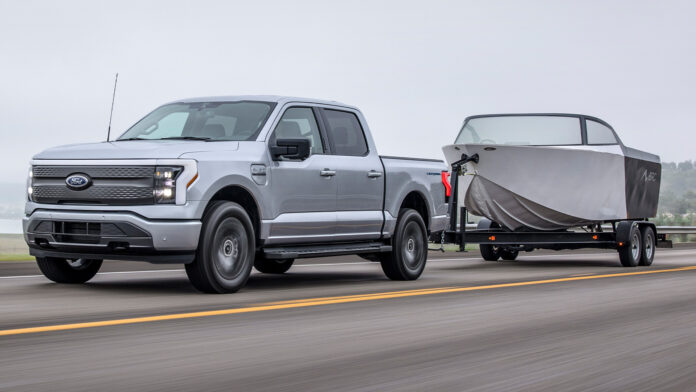 A Ford F-150 Lightning tows a boat down the highway.